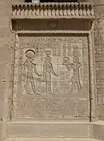Relief auf einer Stellwand zwischen Säulen in Dendera, mit Abbildungen von Sumpfpflanzen am Sockel, Torusleisten, die das Relief einrahmen, und einem Hohlkehlgesims mit einem Flügelsonnesemblem, das von einem Fries aus Uräen gekrönt wird. Erstes bis zweites Jahrhundert n. Chr.