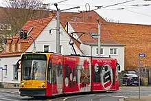 Dreiteiliger Straßenbahnwagen mit roter Vollwerbung. In der Zielanzeige steht in grüner Schrift "5 Nordhausen Ost".
