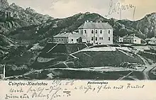 Hier ist eine Postkarte zu sehen die ein sehr großes Haus in hügeliger Landschaft zeigt.