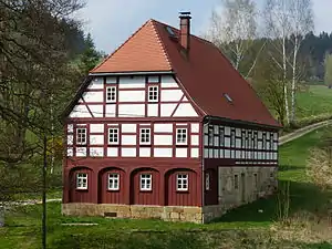 Schrägaufnahme eines Fachwerkhauses, der Saupsdorfer Hütte, im Grünen gelegen mit einigen Bäumen im Hintergrund
