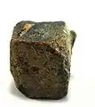 Rutherfordin (gelblichbrauner Belag) auf Uraninit aus dem Ulugurugebirge, Tansania (0,9 cm × 0,8 cm × 0,7 cm)