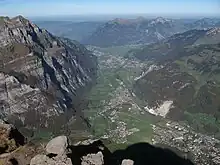 Ansicht von Süden; links Aufschwung zu Wiggis und Rautispitz. Orte: Rechts unten Glarus, links erst Riedern, dann Netstal, Mollis/Näfels und Niederurnen am Talausgang