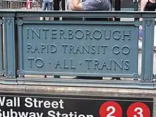 Detail eines Bahnhofseingang: Ein Blechschild als Teil der Brüstung, mit der dreizeiligen Inschrift „Interborough / Rapid Transit Co / To All Trains“