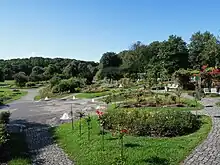 Ein halbrund an einem leichten Hang angelegter Rosengarten, im Vordergrund ein Brunnen