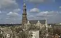Seitliche Farbfotografie in der Obersicht einer braunen Kirche mit weißen Ornamenten um das Kirchenschiff und den Dachgiebeln. Der Turm mit goldener Haube und Dachlaterne steht links.
