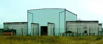 Südansicht der für die nie realisierten HGÜ-Kurzkupplung Wolmirstedt errichteten Stromrichterhalle; zwischen den Betonwänden im Vordergrund sollte die Glättungsdrossel installiert werden, über den mit Schienen versehenen Betonweg war der Antransport schwerer Komponenten geplant