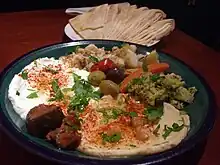Joghurt und Hummus mit frittiertem Gemüse auf einem blauen Keramikteller mit Fladenbrot auf einem kleinen weißen Teller daneben
