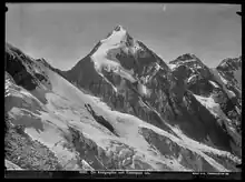 Schwarz-weiß Fotografie eines spitzen Berggipfels mit Schnee und Eismassen auf dunklem Fels