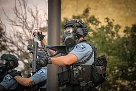 Polizist mit Atemschutzmaske beim Verschießen von Tränengasgranaten